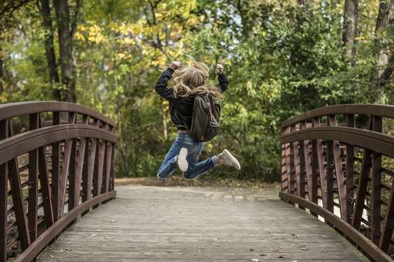Springende Schülerin mit Rucksack auf Brücke