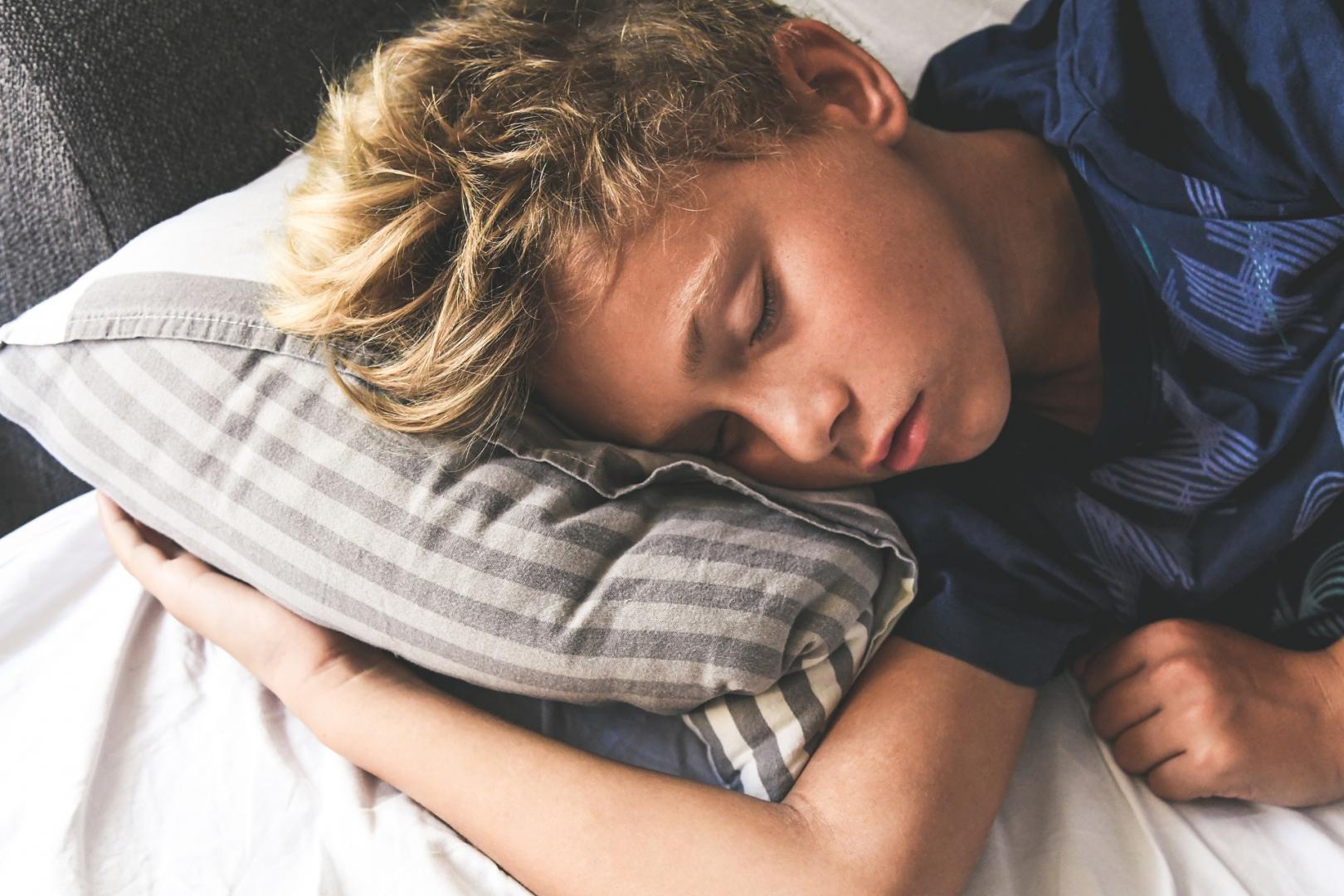 Junge im blauen T-Shirt schläft in seinem Bett